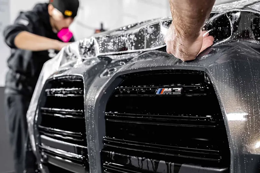 Technician installing clear paint protection film on a BMW M3 hood