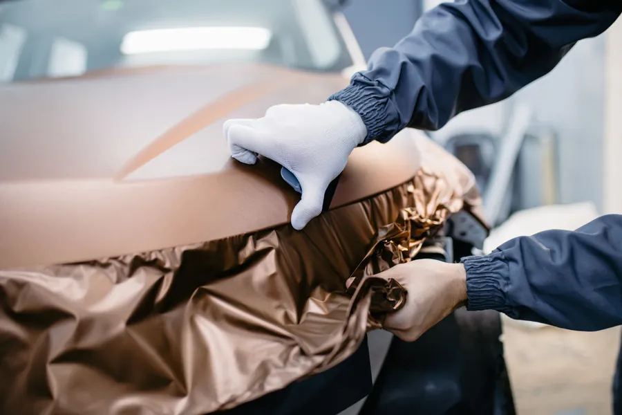 Installer wrapping a vehicle hood in bronze vinyl